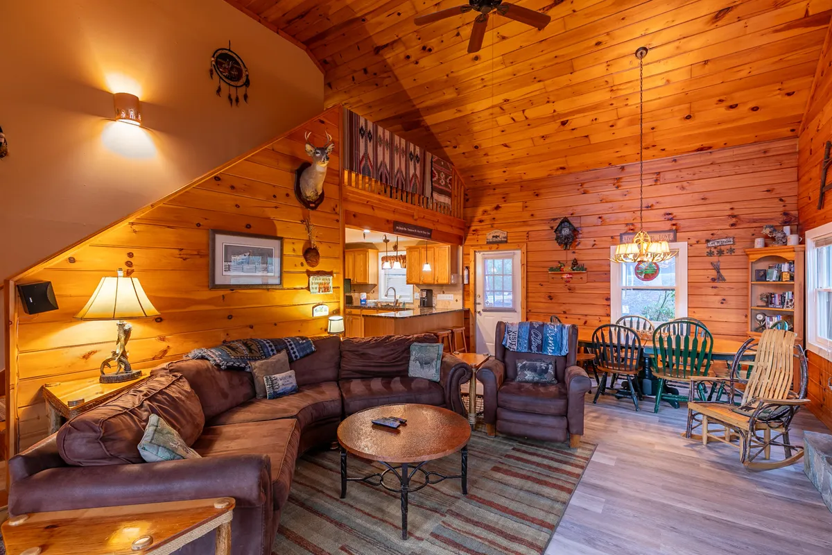 A spacious interior scene featuring a large sectional sofa perfect for movie nights, a rustic dining table primed for group meals or games, and prominent wooden accents that evoke a mountain retreat ambiance. The lighting creates a soft, welcoming mood ideal for family or group connections.