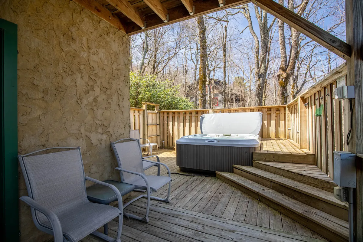 This exterior shot features a private hot tub on a wooden deck, surrounded by trees with two chairs positioned for relaxation. The tranquil outdoor setting is perfect for stargazing, soaking, or sharing a quiet moment amidst nature.