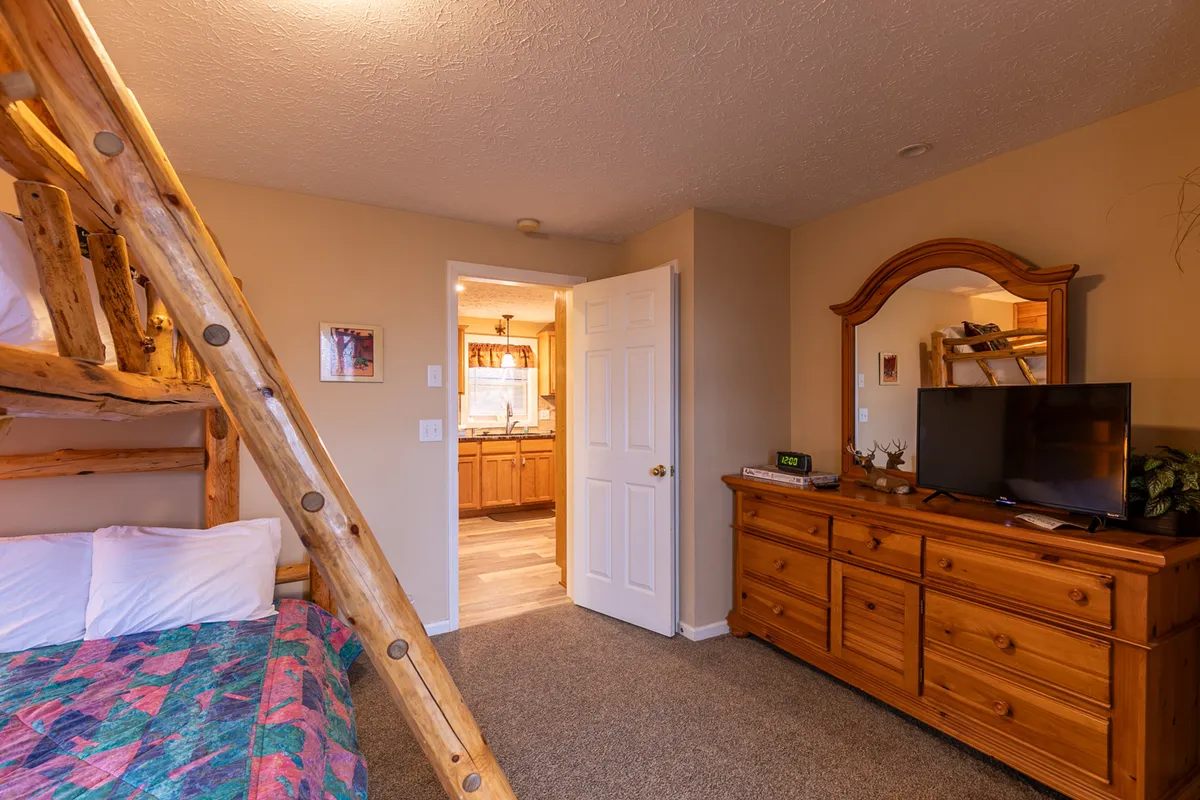 A versatile room with a bunk bed, dresser, TV, and mirror, arranged for both rest and entertainment. The room is bright and inviting, suitable for kids and adults alike, hinting at family game nights or quiet downtime after a day of adventure.
