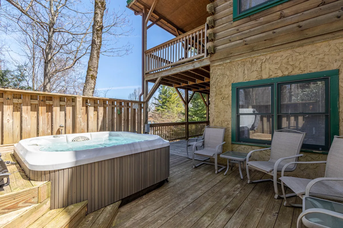 Centered on a privacy-screened hot tub nestled on a wooden deck, this image is surrounded by lush green trees and offers seating for relaxing or socializing. The mood is tranquil and inviting, with hints of sunset colors filtering through and the promise of stargazing at night.