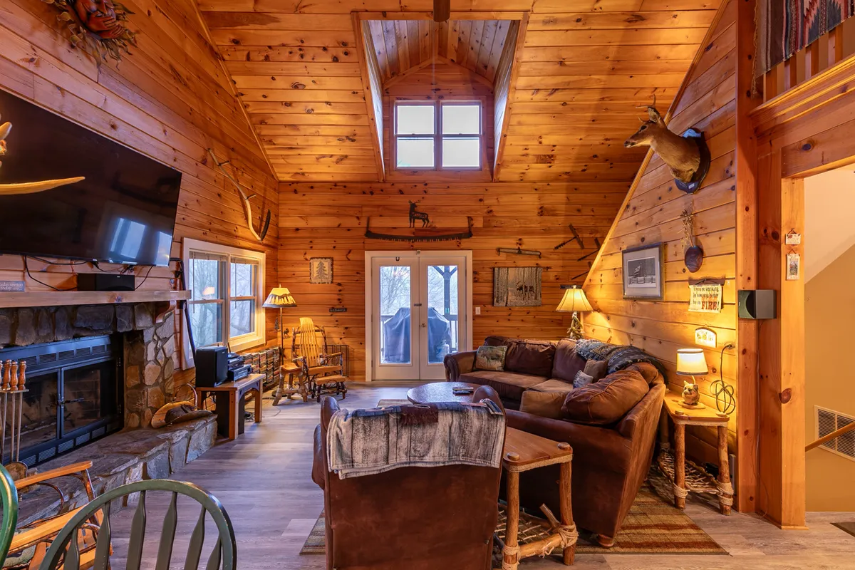 A spacious living area with a large stone fireplace, cozy sofa, and expansive windows framing the outdoors. The room is filled with natural light, wooden beams overhead, and views of surrounding greenery, inviting both people and pets to settle in after a day of adventure.