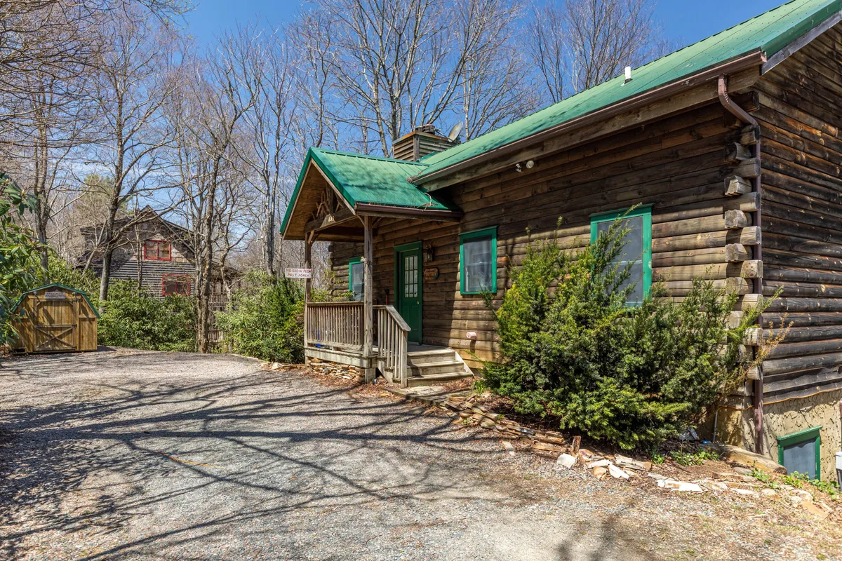 This image shows a charming log cabin with a green roof, a wooden porch, and lush trees surrounding the structure. The setting evokes a sense of cozy seclusion and adventure, suggesting easy access to nearby nature trails and a restful home base after a day of exploration.