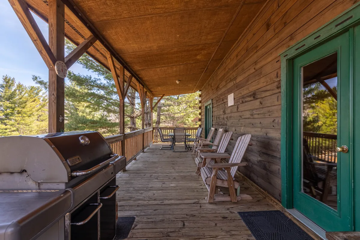 This image features a grill set up on a wooden deck, flanked by classic rocking chairs and a sturdy wooden railing. The scene hints at outdoor cooking, relaxed seating, and a natural backdrop ideal for gatherings, barbecues, and enjoying the outdoors.