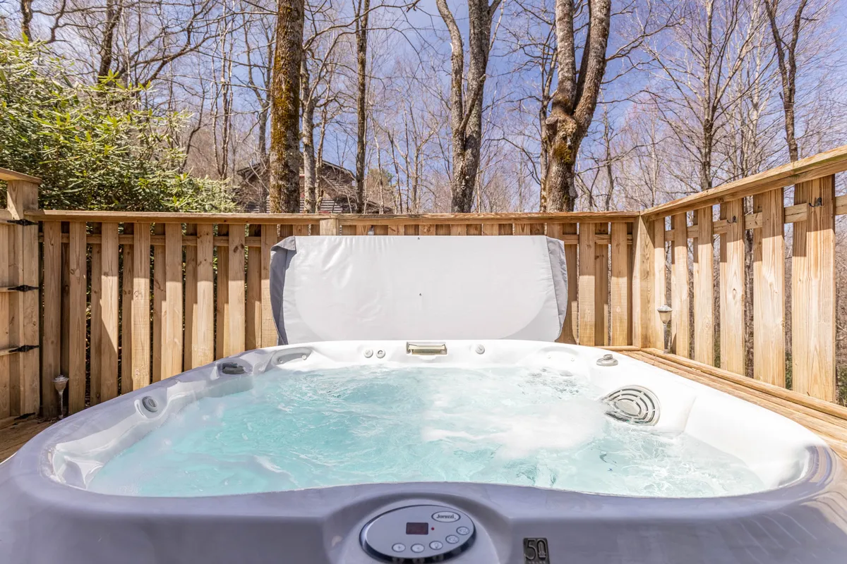 A wooden deck with a bubbling hot tub set against a backdrop of lush trees, creating a peaceful, secluded atmosphere ideal for relaxing or socializing after an active day outdoors.