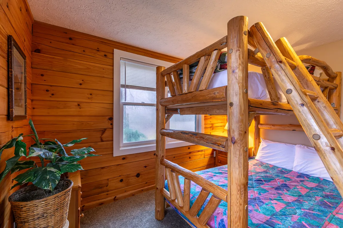 A cozy bunk bed set against a wooden wall, with a window that lets in natural light and a potted plant adding a touch of cheer. The playful sleeping arrangement is ideal for kids, evoking memories of family vacations and indoor bonding.
