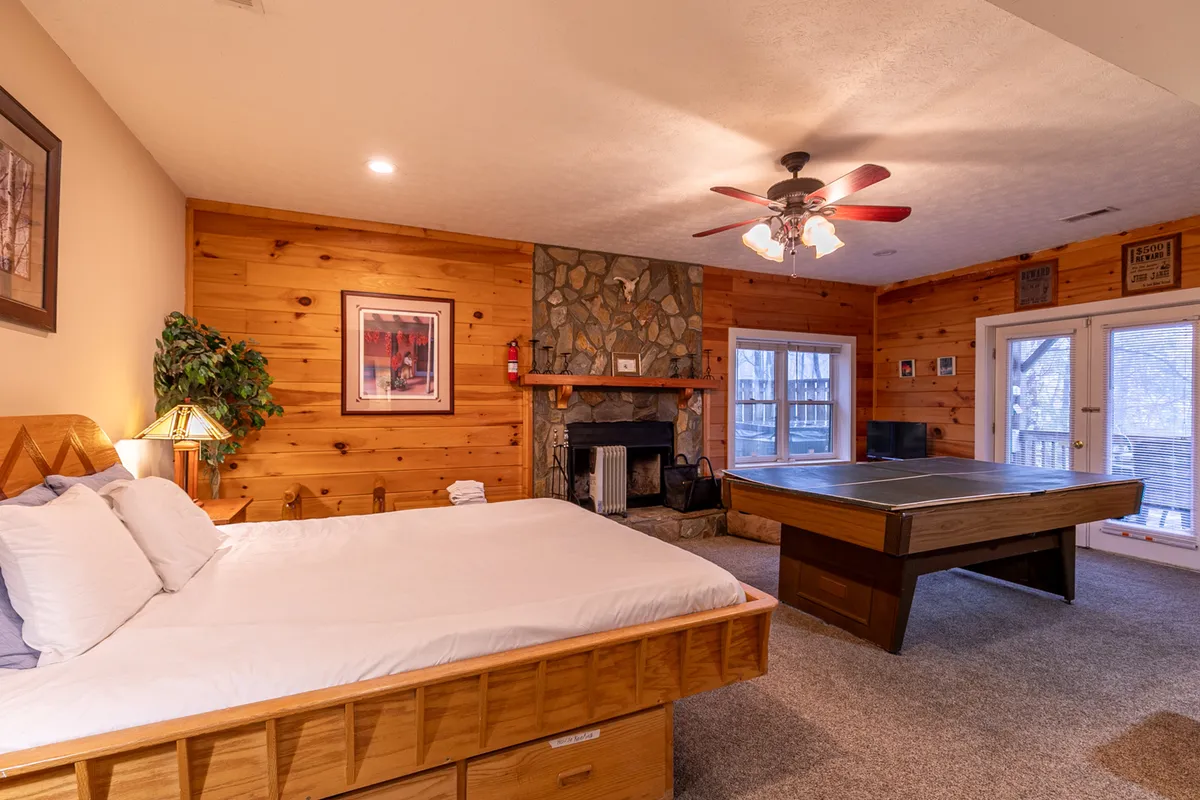 A master suite featuring a comfortable bed positioned near a stone fireplace, with a game table and large windows that let in natural light. The space feels private and inviting, perfect for relaxation and private moments. The presence of the fireplace, bed, and lounge area aligns with the master suite described in the content.